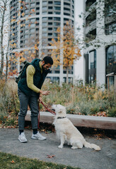 Side view of happy young man training his dog outdoors in city.