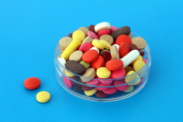 There are many multi-colored pills on a transparent bowl.