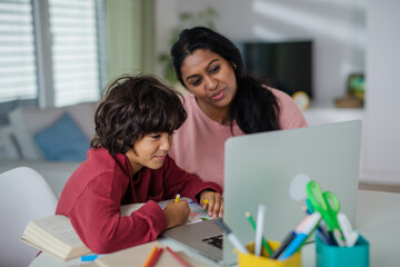 Indian mother with little son using laptop and having online school lesson at home.