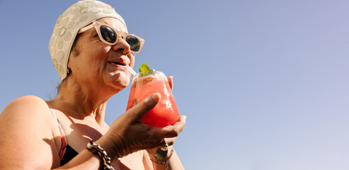 Elderly woman drinking a tiki cocktail in the summer