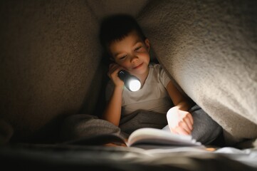 Child reading book in bed. Kids read at night. Little boy with fairy tale books in bedroom . Education for young children. Bedtime story in the evening. Cute kid under blanket in dark room with lamp.