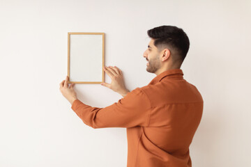 Young man hanging picture frame on the wall