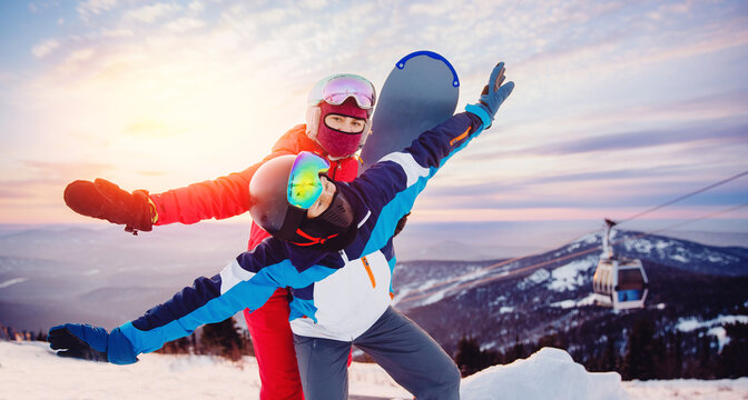 Happy lovers couple man and young women snowboarders on background of ski resort sunset. Concept banner winter sports Alps