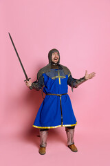 Full-length portrait of man brave medieval warrior or knight in chain armor with sword screamimg...