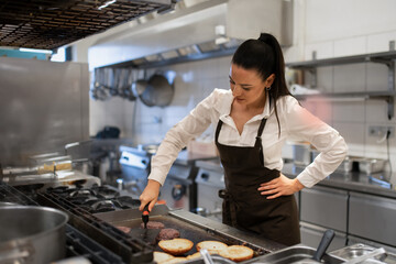 Professional female chef preparing meal indoors in restaurant kitchen.