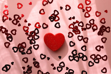Small red heart and heart shaped confetti on pastel pink background. Flat lay.