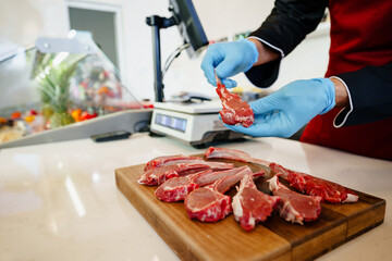 Young butcher holding raw lamb ribs in a butcher shop