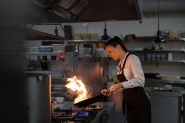 Professional chef preparing meal, flambing indoors in restaurant kitchen.