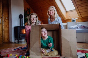 Boy with Down syndrome with his mother and grandmother playing with box together at home.