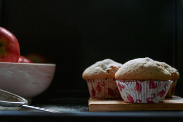 Rustikale Apfel Muffin frisch aus dem heimischen Offen . Das Zuckersieb liegt noch neben einen Holzbrett auf dem die Muffin angerichtet sind ,das ganze ist mit Zucker bestreut und auch noch köstliche 