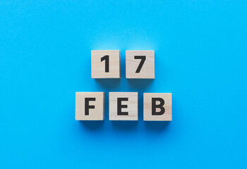 Text 17 FEB (FEBRUARY) on wooden cubes on BLUE background. Date.  Square wood blocks. Top view, flat lay.