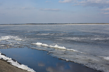Winter landscape with partly frozen river. Ice floes float on the blue surface. Ice drift. Global warming concept.