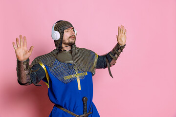 Portrait of man, medieval warrior or knight listening to music in headphones and dancing isolated...