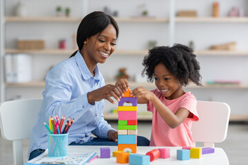 Adorable black kid and child development specialist playing with bricks