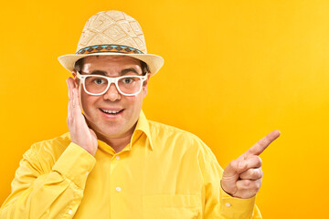 Funny fat man tourist in hat and glasses with surprised face spreads arms on yellow studio background