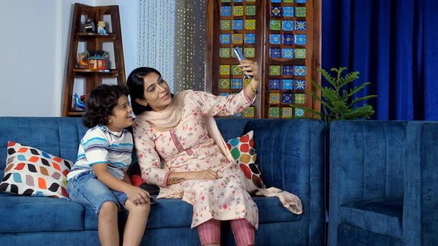 Beautiful Indian mother and her cute son talking on a video call - modern technology. A little kid in casual clothes happily waving his hand while chatting online - distant communication  leisure t...