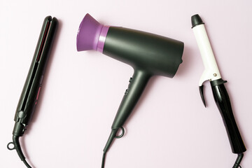 Fototapeta premium hair dryer, curling iron, straightener in black on purple background, professional hairdresser set