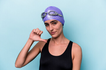 Young swimmer woman isolated on blue background showing a dislike gesture, thumbs down. Disagreement concept.