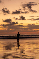 Fototapeta premium vertical portrait, Silhouette of a woman enjoying a sunset on a beach in Costa Rica.