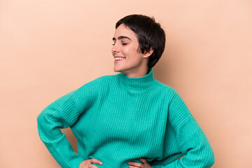 Young caucasian woman isolated on beige background laughs happily and has fun keeping hands on stomach.