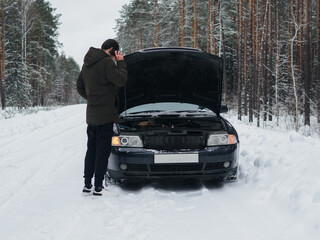 A car breakdown on a snowy winter road. Male driver uses phone to call tow truck or help