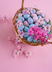 Fototapeta na wymiar Wicker basket with chocolat eggs and spring bright flowers, selective focus. Geeting card for the celebration of Easter, copy space
