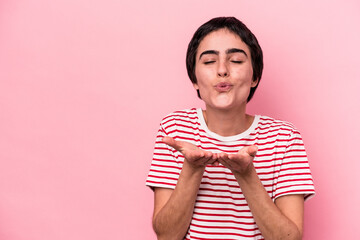 Young caucasian woman isolated on pink background folding lips and holding palms to send air kiss.