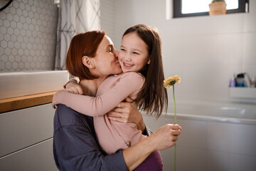 Little girl congratulates mother and gives her flower in bathroom at home.