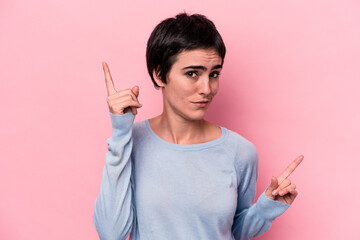 Young caucasian woman isolated on pink background pointing to different copy spaces, choosing one of them, showing with finger.