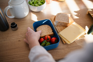 Close-up of mother preparing snack to lunch box in kitchen at home.