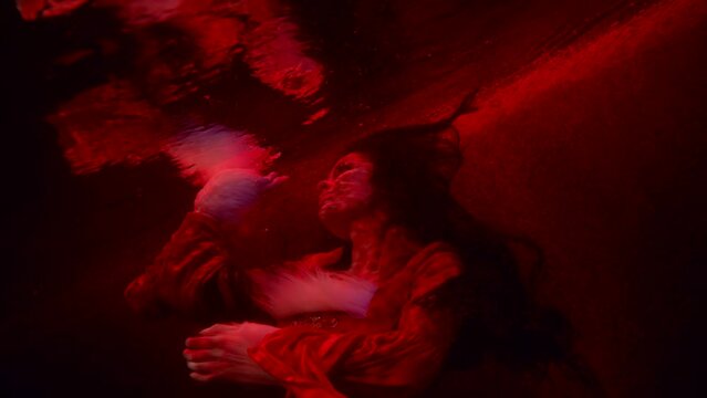 sexy woman is floating under water surface in enigmatic red light, sensuality and femininity
