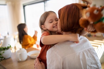 Rear view of mother hugging her little daughter in kitchen at home.