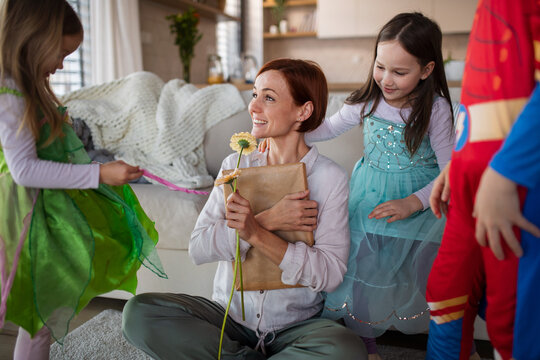 Mother of three little children in costumes getting present and flower from them at home.