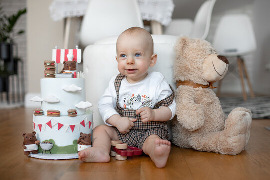 tiny adorable child sitting on floor near the birthday cake and teddy bear. Looking with sad eyes. Close-up photo