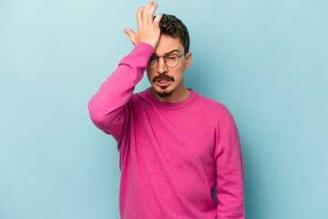 Young caucasian man isolated on blue background forgetting something, slapping forehead with palm...