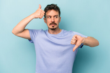 Young caucasian man isolated on blue background showing thumbs up and thumbs down, difficult choose...