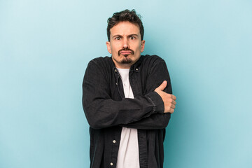 Young caucasian man isolated on blue background shrugs shoulders and open eyes confused.
