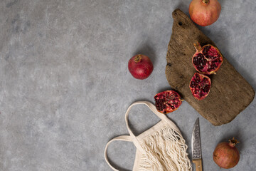 Beautiful red pomegranate fruit composition on a concrete background. Half pomegranate and ripe pomegranate fruit with rustic wooden board, knife and string bag. Top view. - 485572698