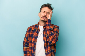 Young caucasian man isolated on blue background tired and very sleepy keeping hand on head.