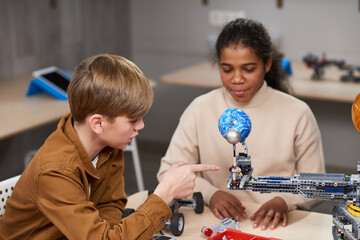 Two teenage kids building electric robots while enjoying engineering class in school, copy space