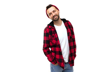 Fototapeta premium a charming man in a red-black plaid shirt and a red hat looks at the camera with a smile on the background of a white wall