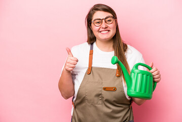 Young gardener caucasian overweight woman holding watering can isolated background smiling and...