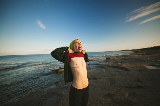 Transgender man standing on coast and showing breast removal scars