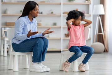 African american woman psychotherapist talking to unruly little girl