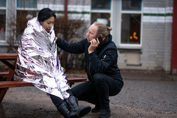 Man calling for ambulance for woman in emergency blanket
