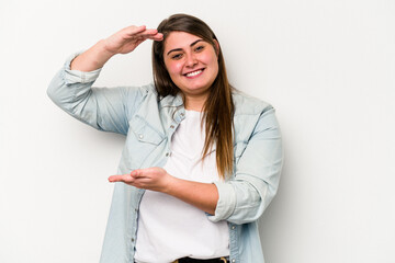 Young caucasian overweight woman isolated on white background holding something little with forefingers, smiling and confident.