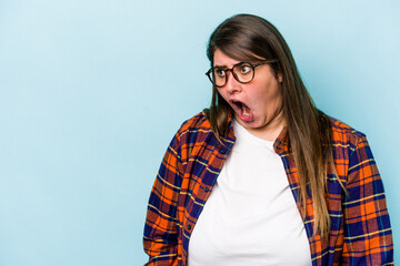 Young caucasian overweight woman isolated on blue background shouting very angry, rage concept, frustrated.