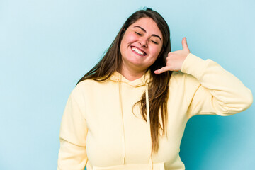 Fototapeta premium Young caucasian overweight woman isolated on blue background showing a mobile phone call gesture with fingers.