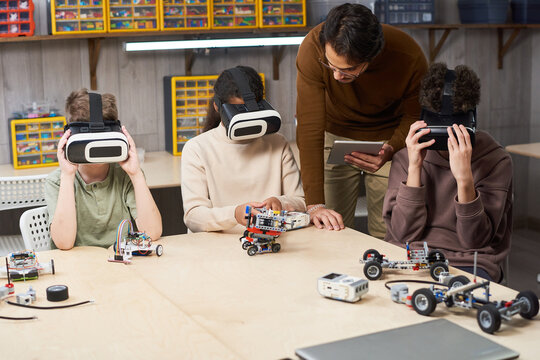 Portrait of male teacher helping group of children wearing VR gear in school and using augmented reality in innovative robotics class - Powered by Adobe