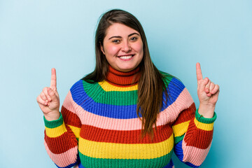 Young caucasian overweight woman isolated on blue background indicates with both fore fingers up...